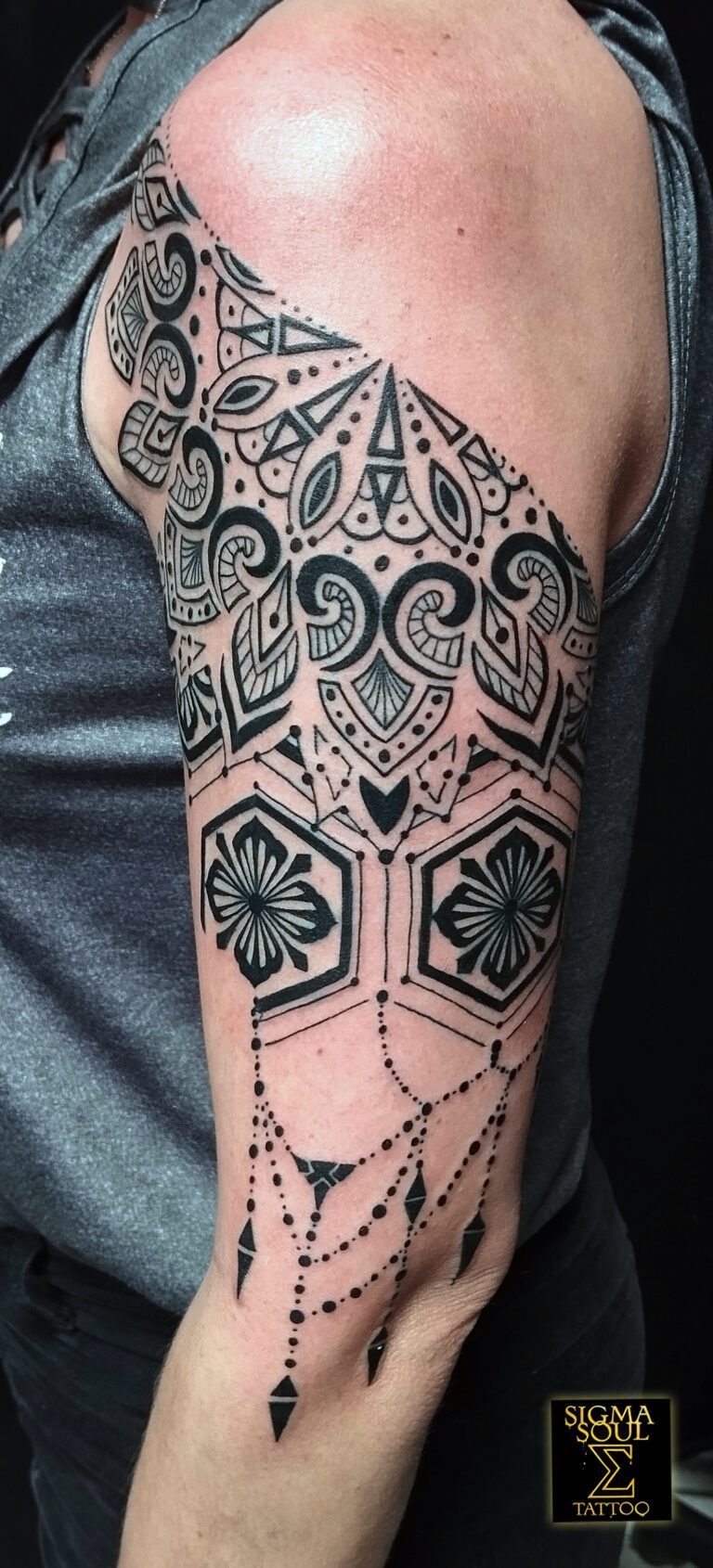Tatuaje geométrico blackwork con patrones andalusíes, florales y ornamentales en hombro y brazo, con cadenas punteadas que simulan joyería. Realizado en Sigma Soul Tattoo en Carmona – Sevilla.