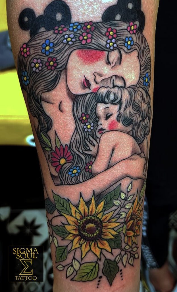Madre eterna. El arte más puro busca permanecer. Esta pieza lo logra con una calma que se siente, no se explica. La figura materna abraza, protege y calla. El trazo es firme, el gesto, ternura. El estilo recuerda al simbolismo de principios del siglo XX: líneas que fluyen, flores que acompañan, colores que respiran calidez. Cada sombra sostiene un vínculo. Cada curva guarda una historia. Sin exceso. Solo intención. El amarillo de los girasoles rompe el silencio con su luz, igual que la presencia de quien da vida. En Sigma Soul Tattoo, el cuerpo se convierte en espacio de memoria. Arte que no se gasta con el tiempo. sigmasoultattoo.com WhatsApp directo: 640 119 066